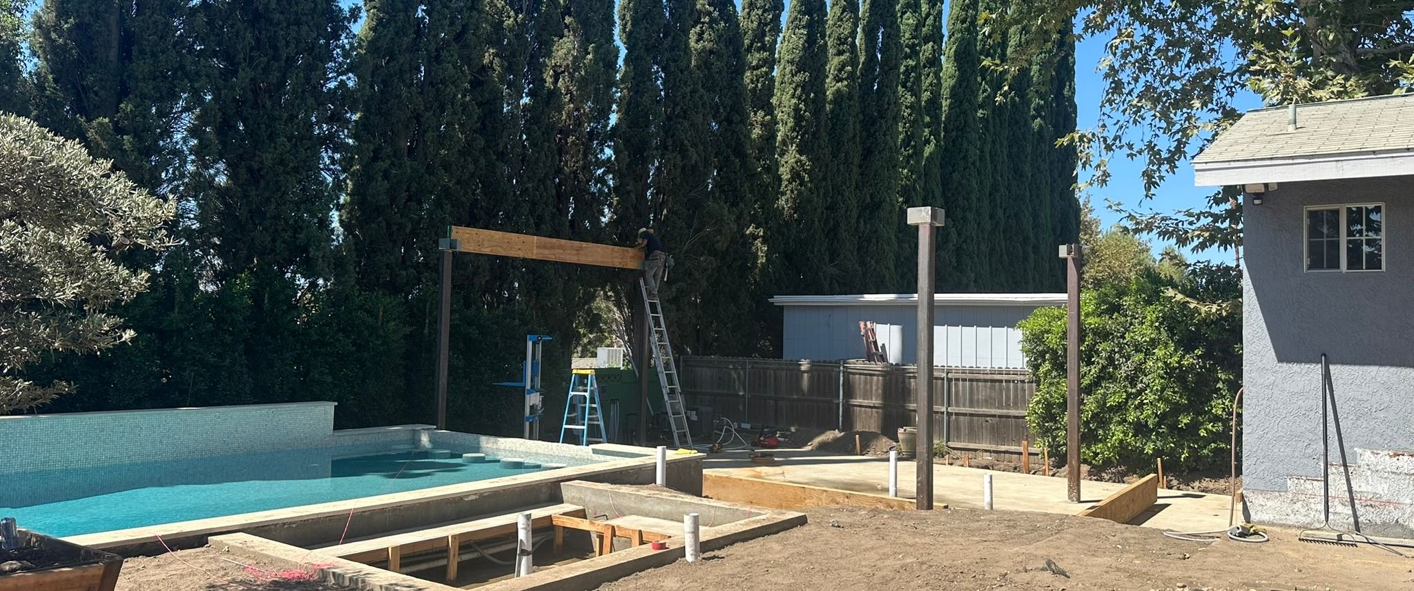 Arnwood — pergola posts and beam raised over the filled pool, under construction